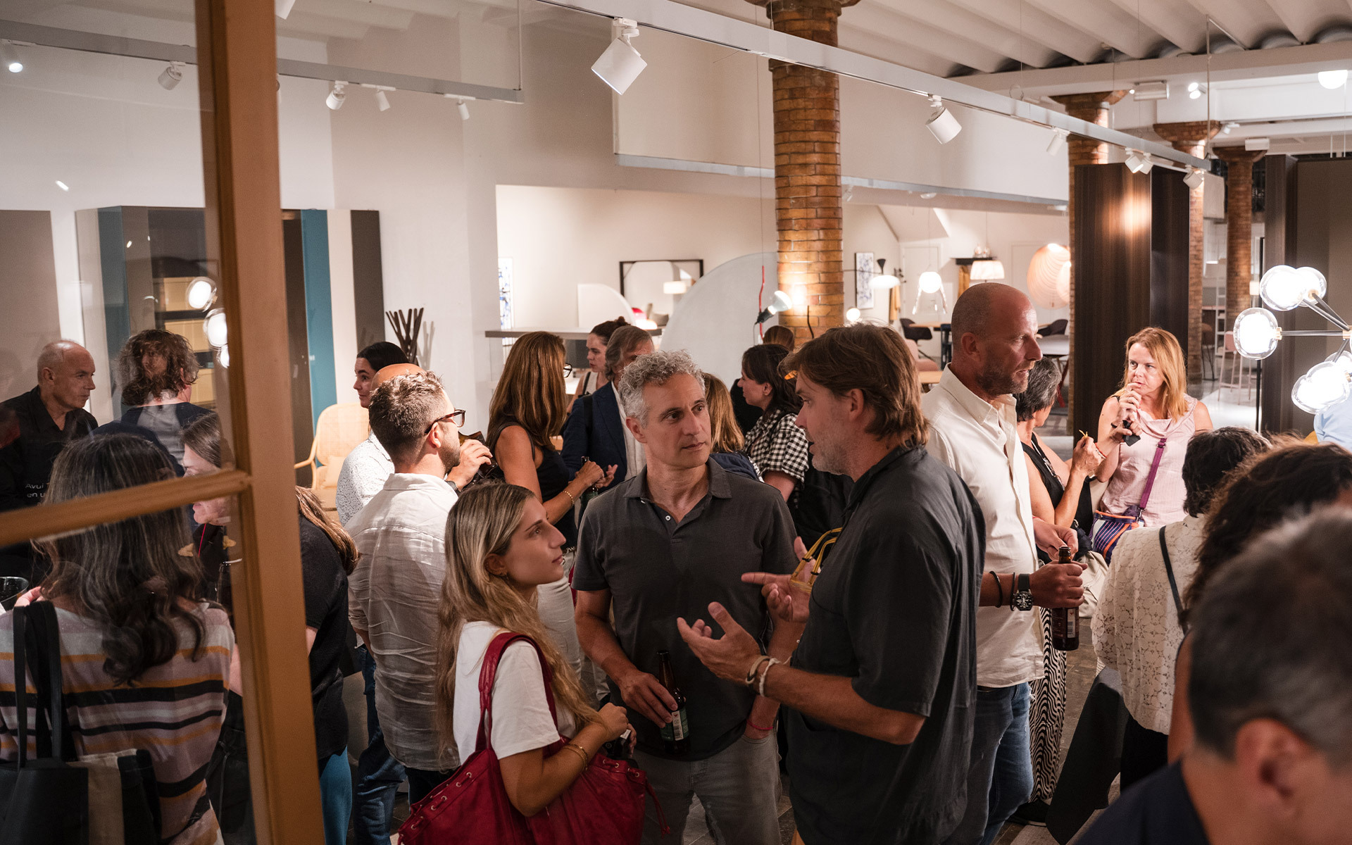 Ospiti che socializzano durante un evento nello showroom Artemide, con varie lampade e apparecchi esposti su pareti e soffitto.