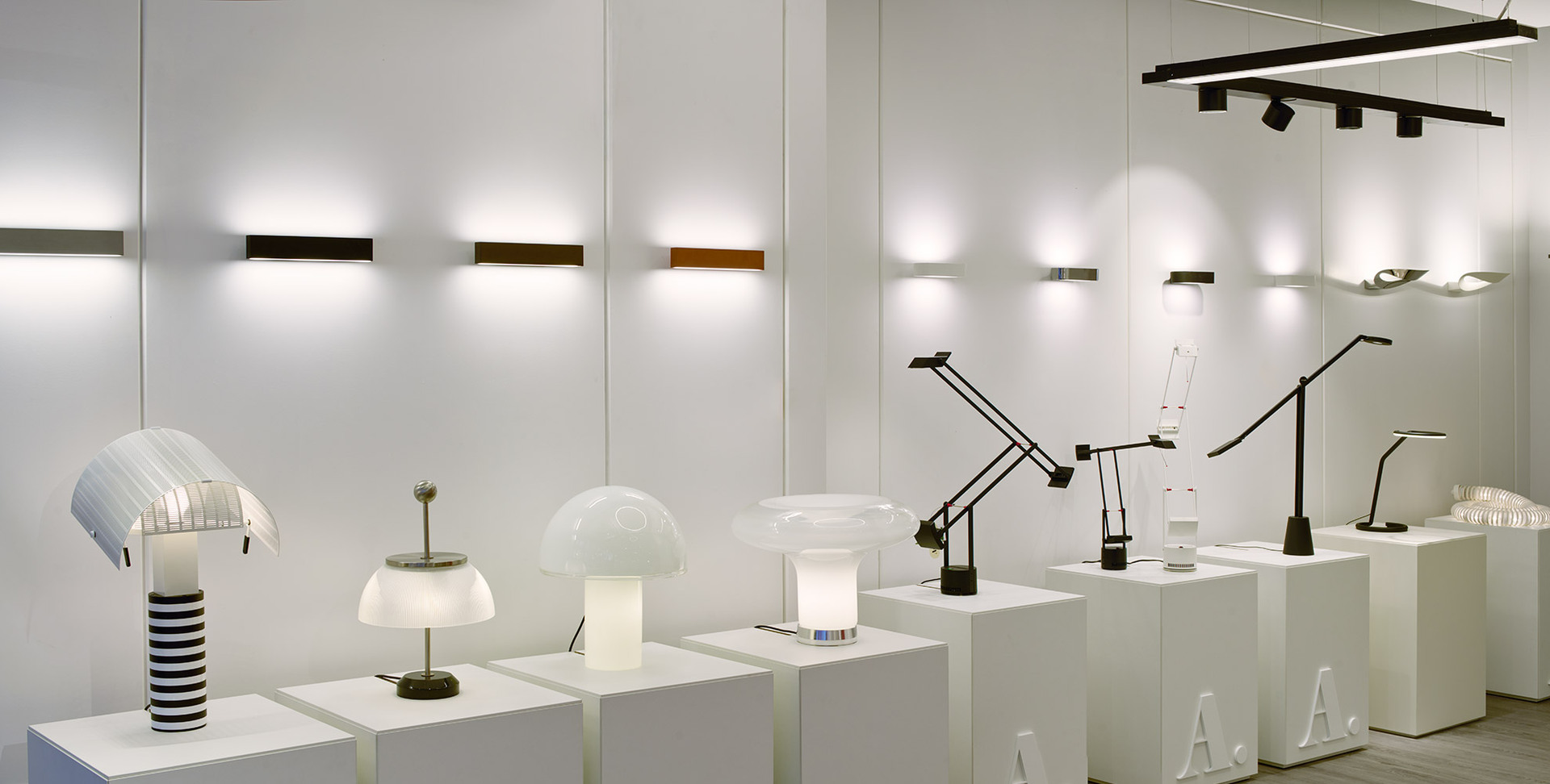 Artemide showroom displaying table lamps, wall lights, and task lamps on white pedestals, bathed in warm ambient lighting