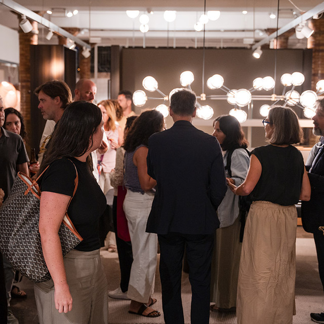 Ospiti che socializzano durante un evento nello showroom Artemide, con un grande lampadario multi-globo che illumina l'elegante spazio.