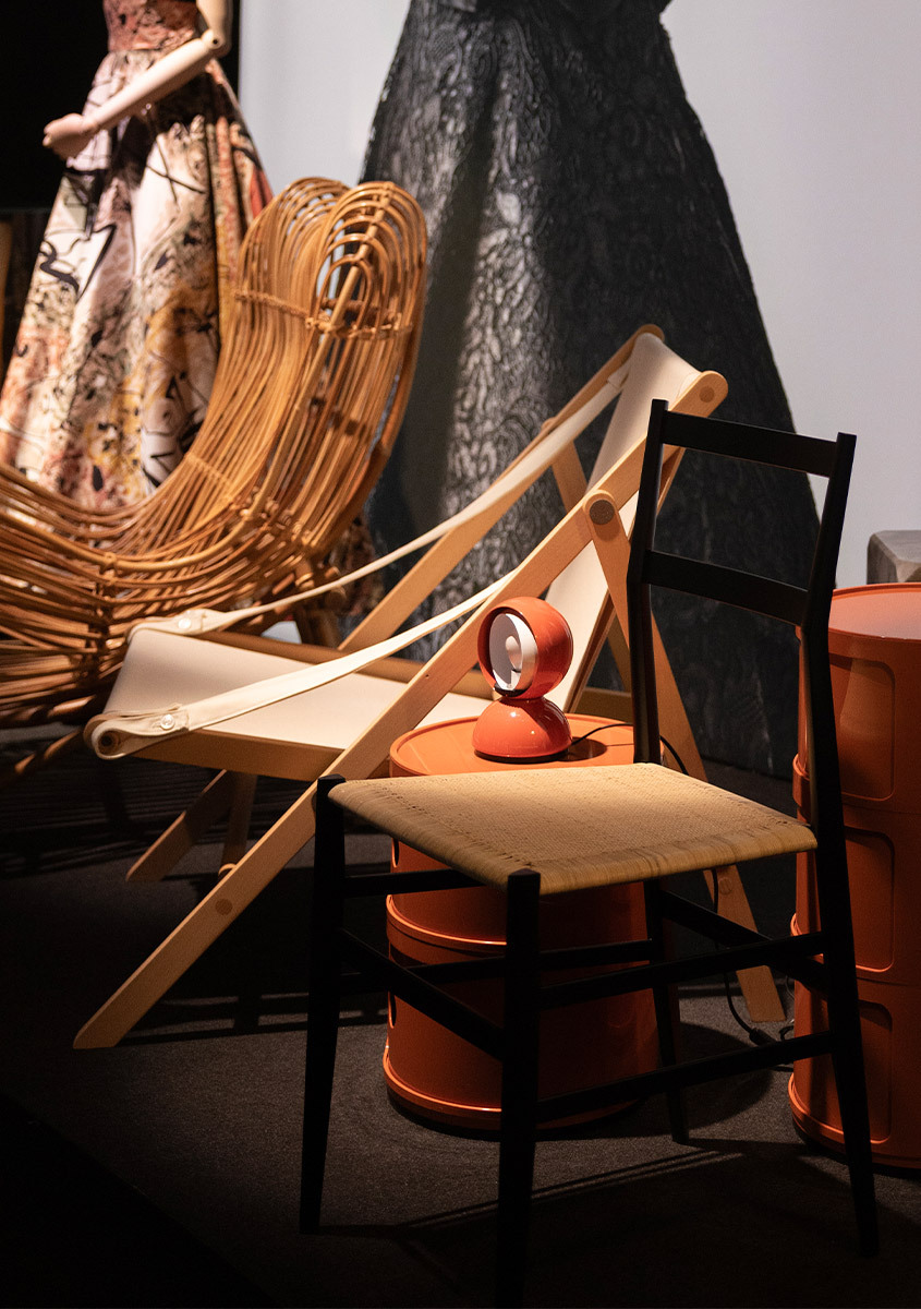 Lampada Artemide Eclisse arancione esposta su un tavolino arancione, accanto a sedute e abiti storici nella mostra ABITO.