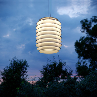 Lampada a sospensione Slicing illuminata in un paesaggio esterno al crepuscolo, con alberi in controluce sullo sfondo