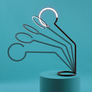 Lampada Vine Light con più profili curvi disposti a ventaglio su un piedistallo azzurro, con un elemento luminoso acceso nella parte superiore. Foto di Pierpaolo Ferrari.