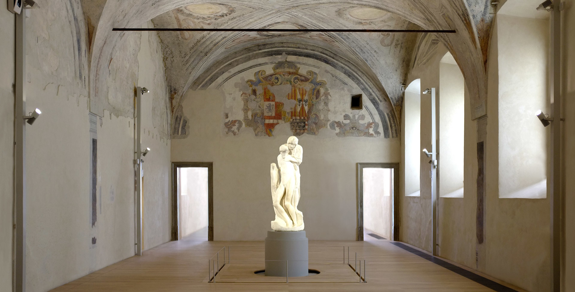 Artemide spotlight illuminates a classical marble sculpture on a pedestal in a historic frescoed hall with vaulted ceiling.