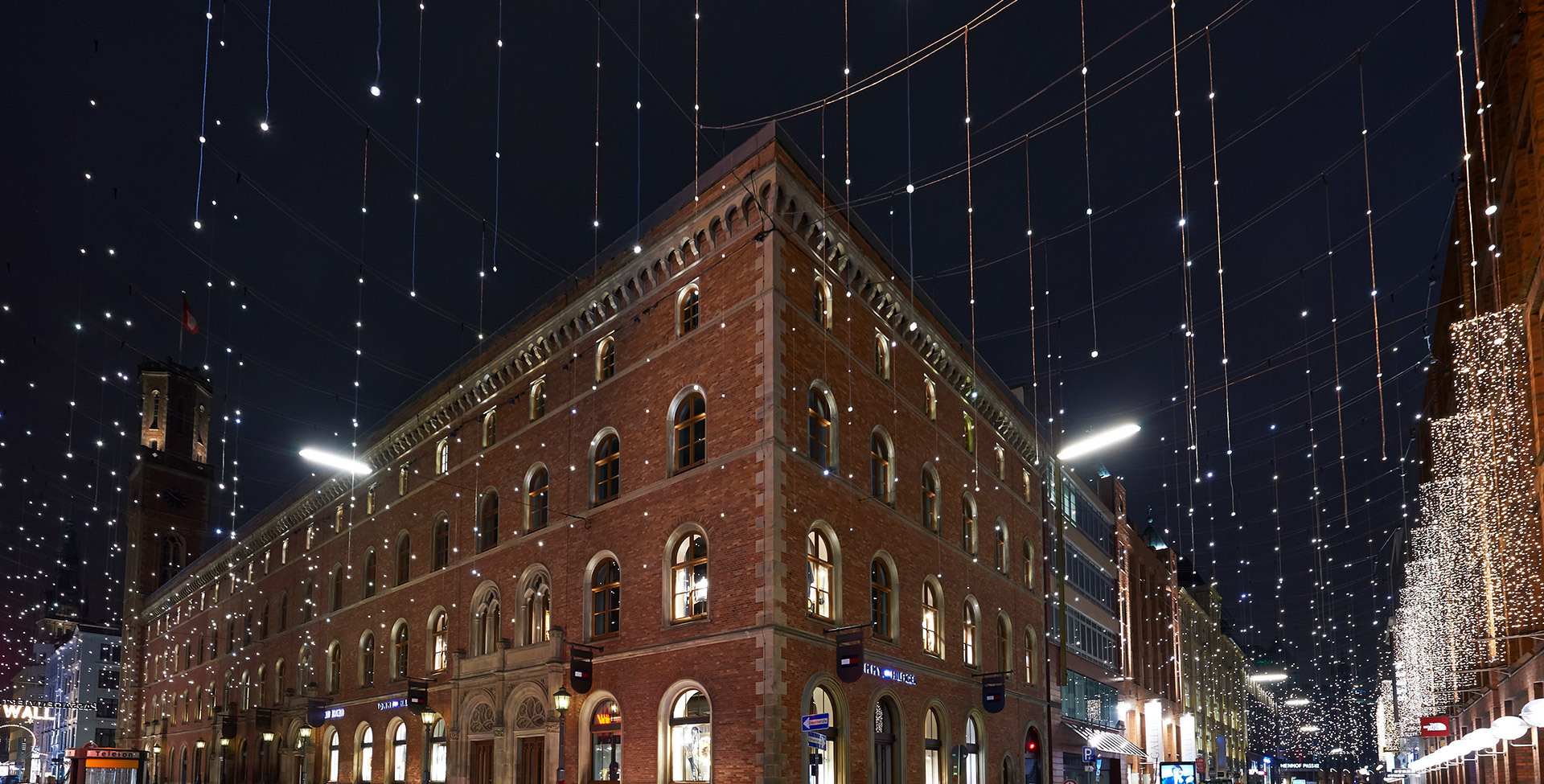 Historic red brick building illuminated at night by street lighting, surrounded by festive hanging lights creating a starry urban atmosphere.