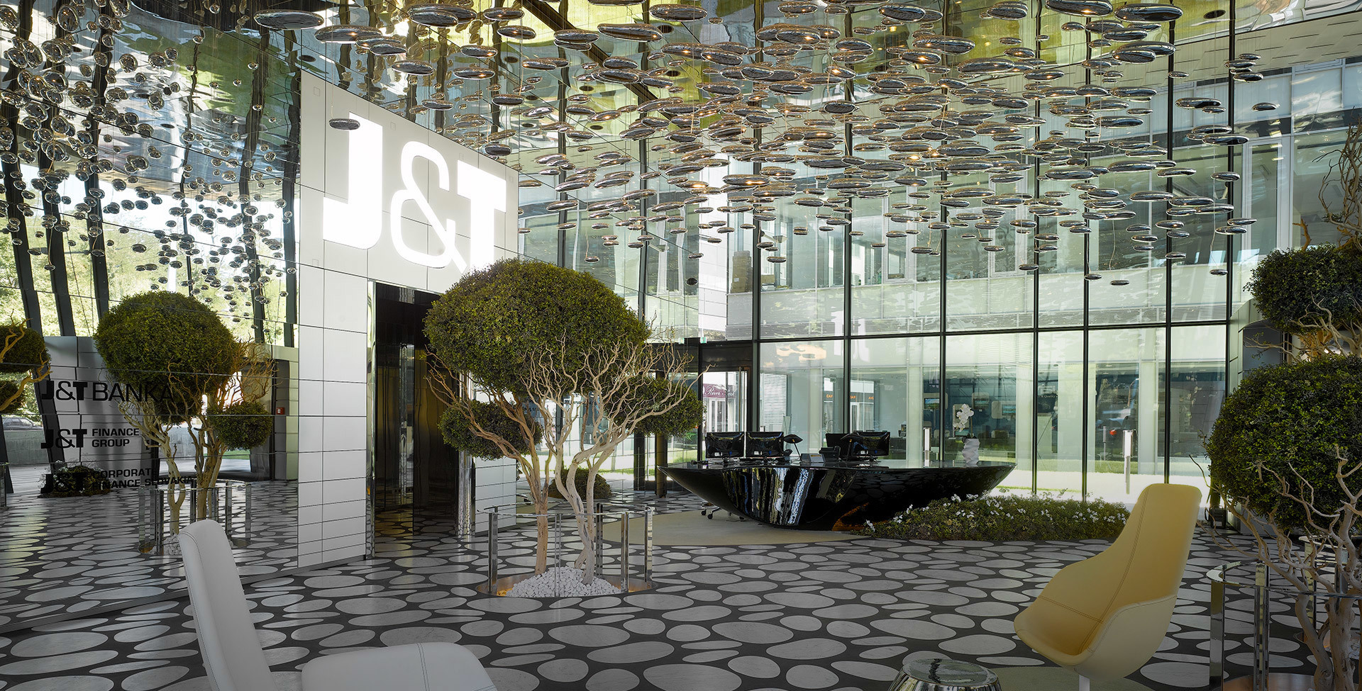 J&T Bank lobby with Artemide pendant lights forming a reflective ceiling installation above manicured trees and modern furnishings