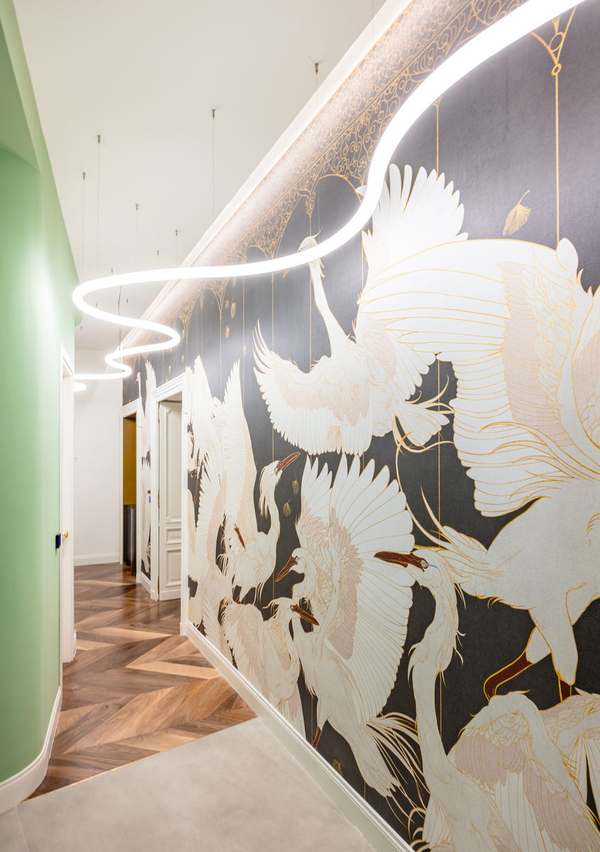 Hallway with circular Artemide pendant lights illuminating a dark wall mural of white and gold herons, herringbone wood floor