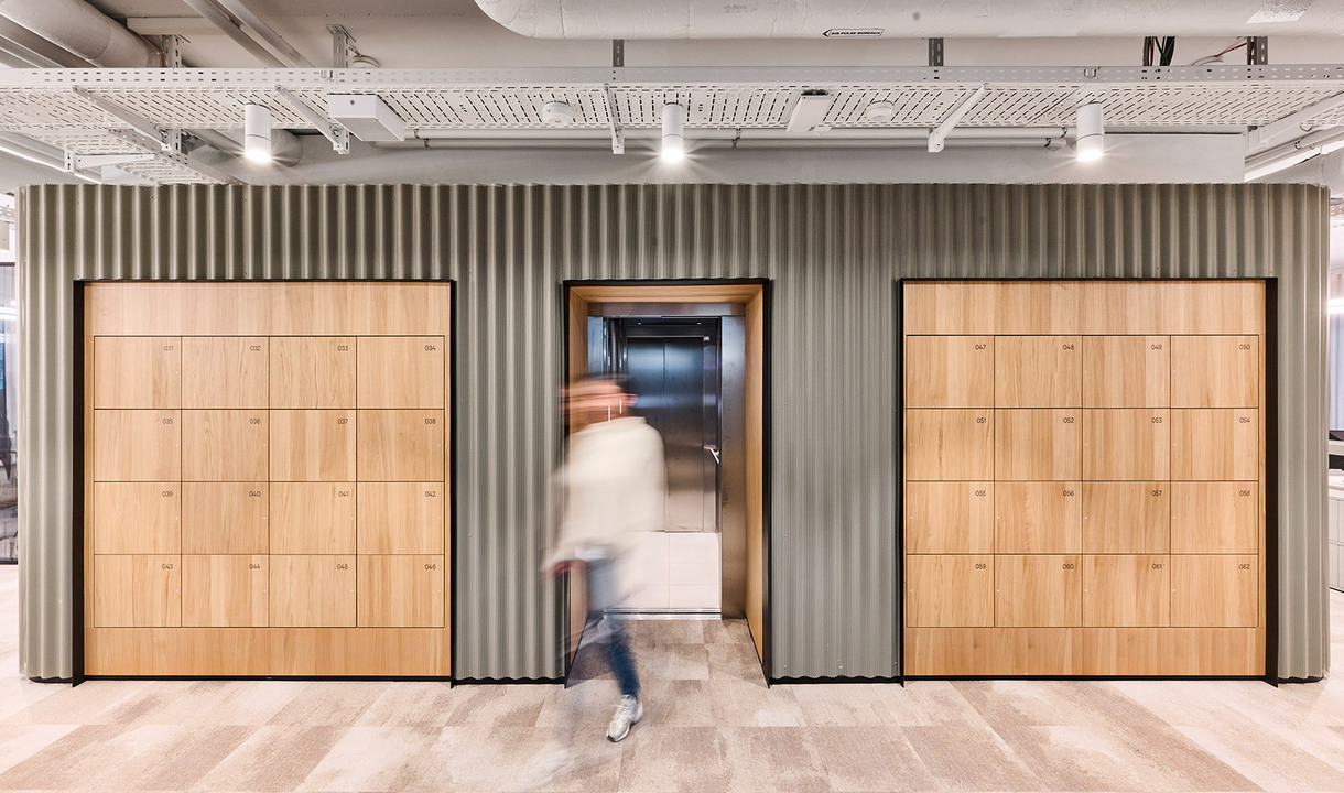 Cloakroom area with wooden lockers and central elevator in a modern corporate space.