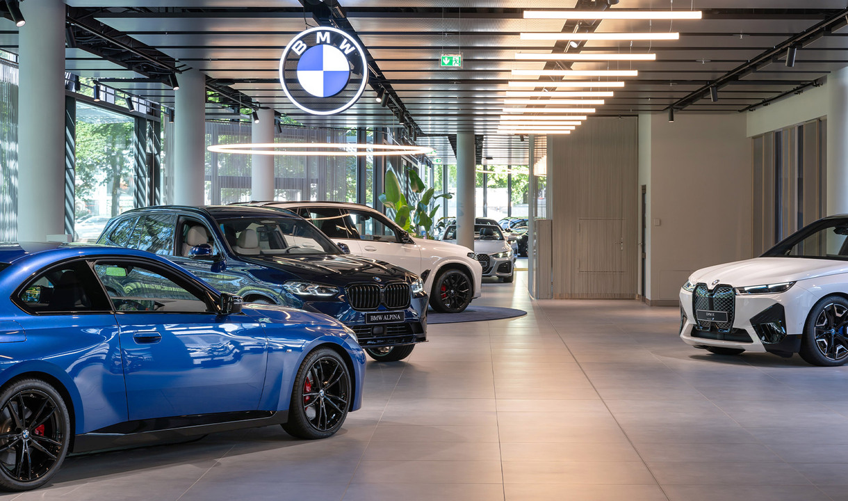 Interno della filiale BMW con più veicoli in fila, illuminato da Alphabet of Light Circular e Linear.