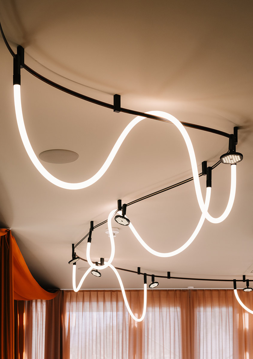 Sylt ceiling system with curved tracks, spotlights, and luminous lines in a lounge setting.
